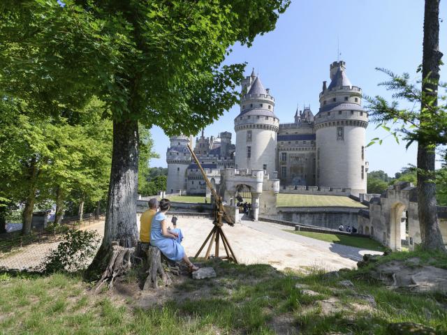 Zwei Personen sitzen an einem Baum und blicken auf Schloss Pierrefonds in Nordfrankreich. Copyright: CRTC Hauts-de-France - Nicolas Bryant